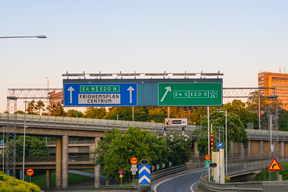 Blue and green prismatic signs mounted on a gantry above the road