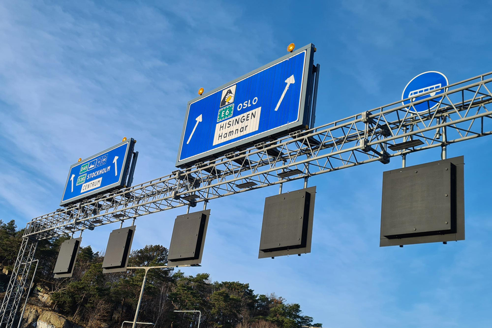 Blue prismatic sign mounted on a gantry above the road